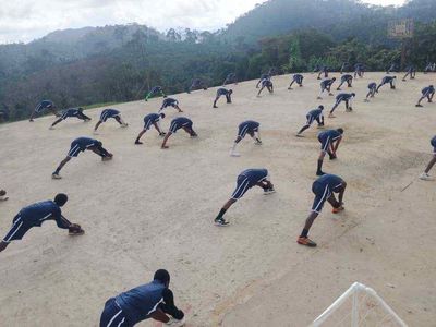 Students in navy sports kit stretching in rows on the hilltop court, forested hills behind